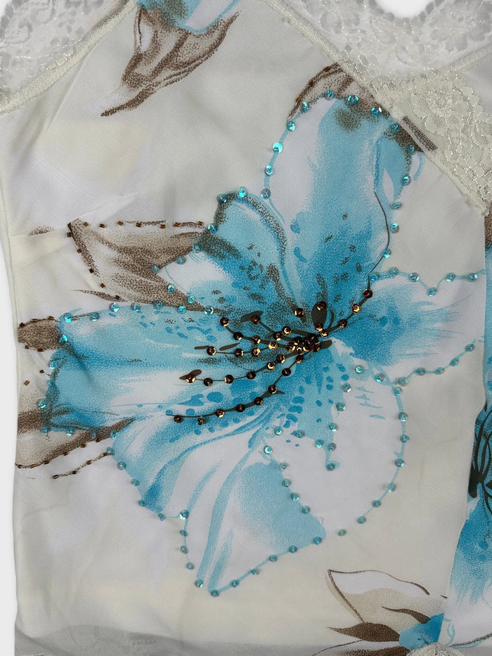 Detail view of a floral women’s top in white and turquoise with embellishments.