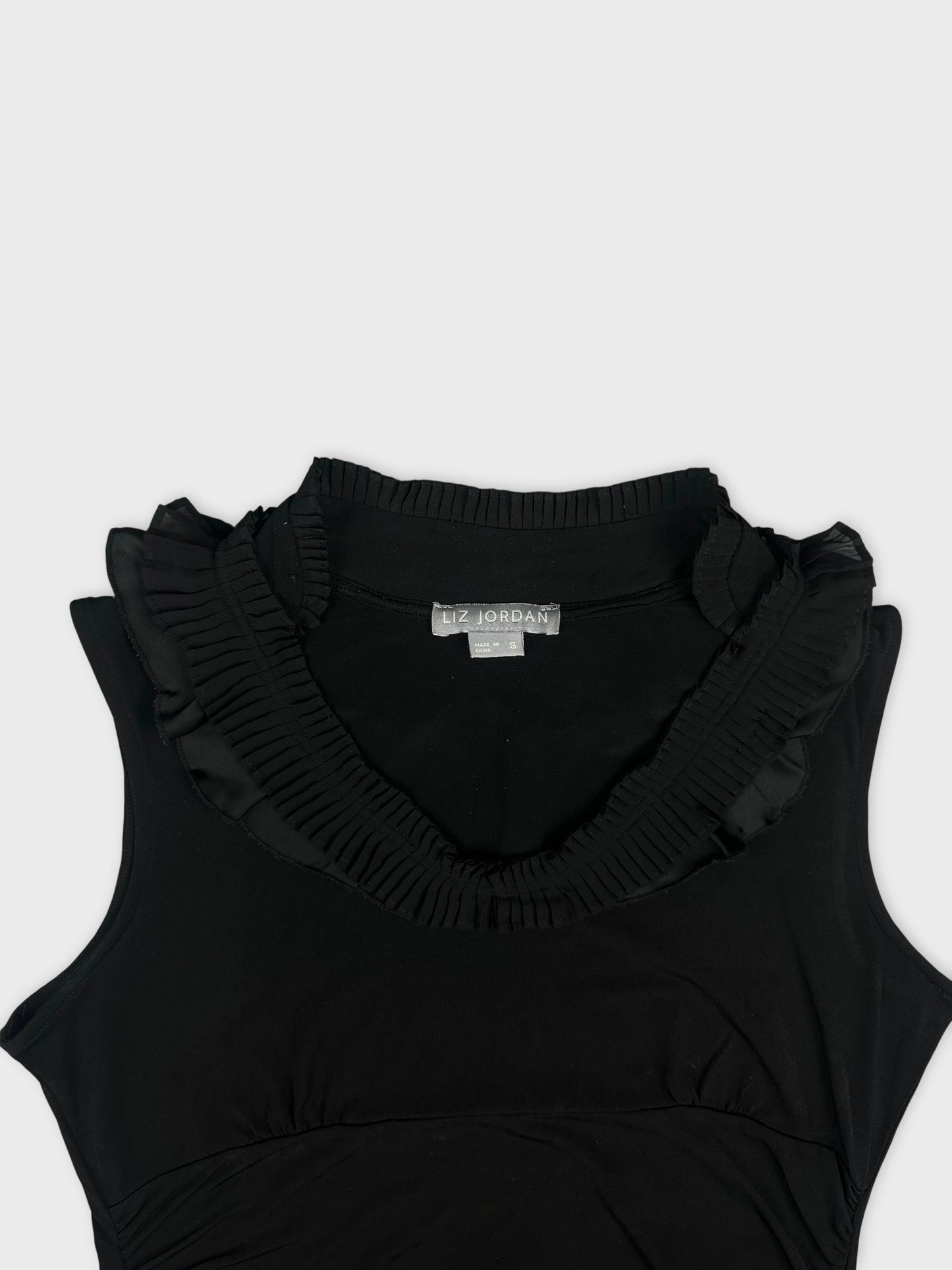 Detail view of a black sleeveless top with ruffled neckline.