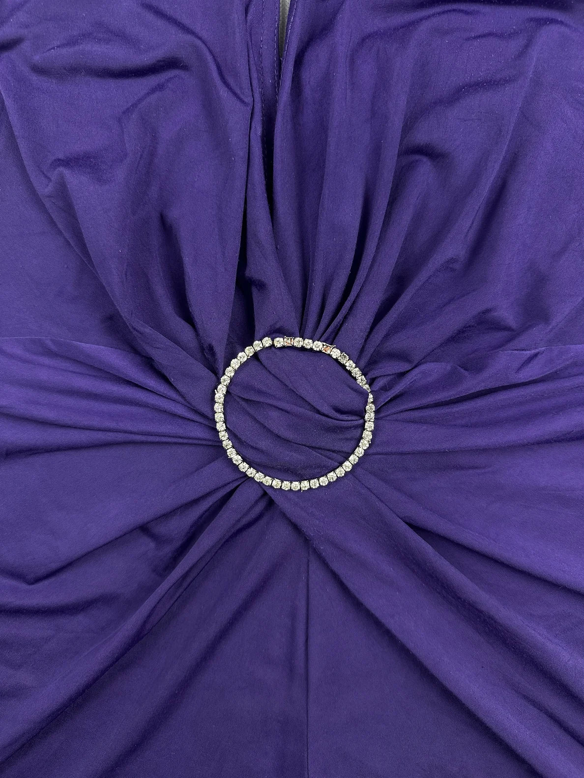 Detail view of a purple women's top featuring a circular rhinestone detail.