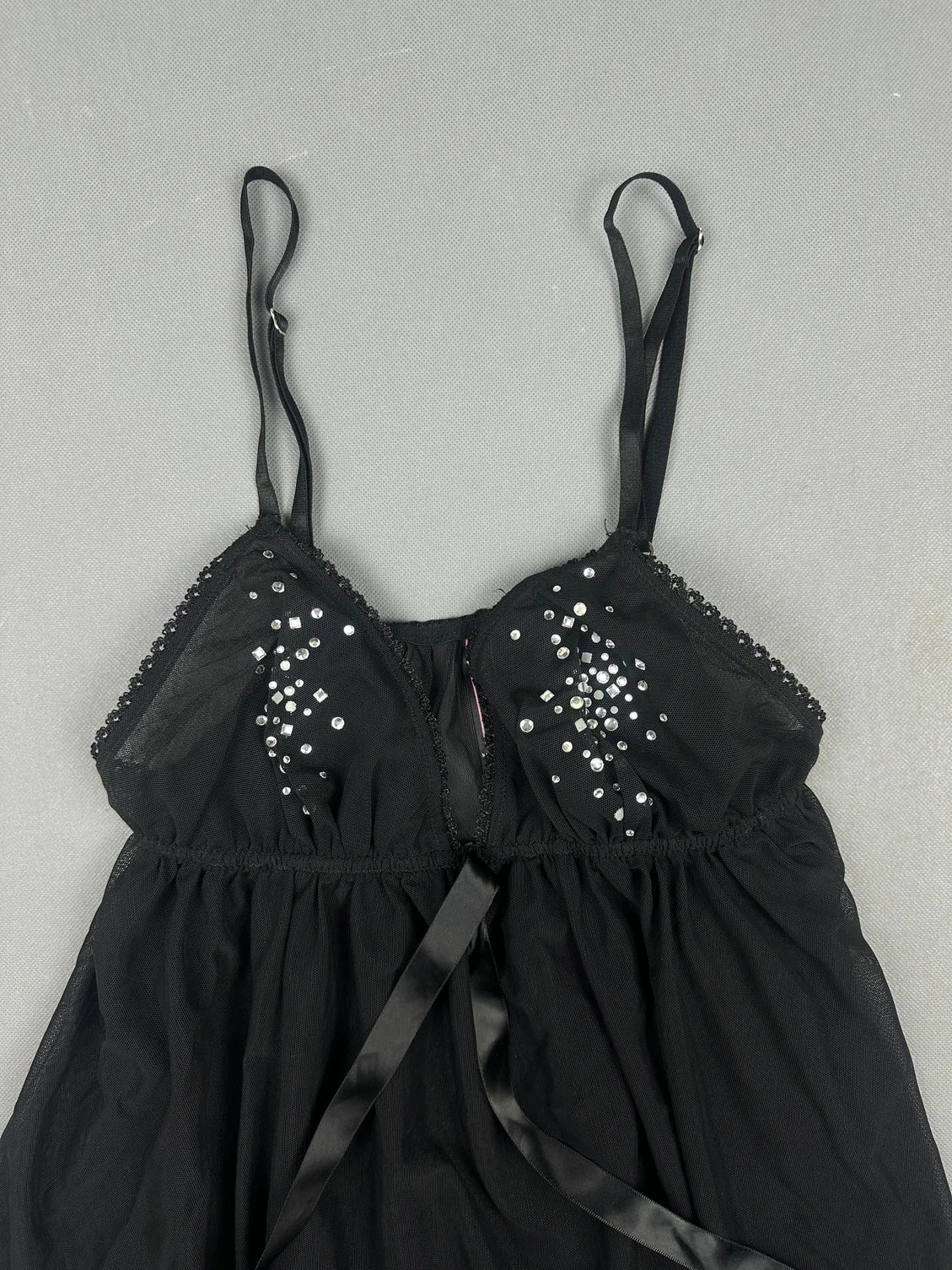 Detail view of a black top featuring rhinestone embellishments and spaghetti straps.