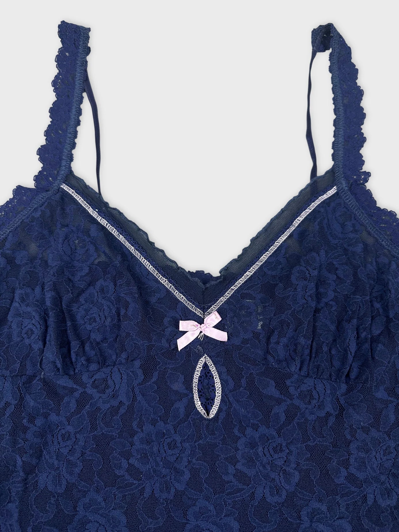 Detail view of a navy blue lace camisole featuring a pink bow.