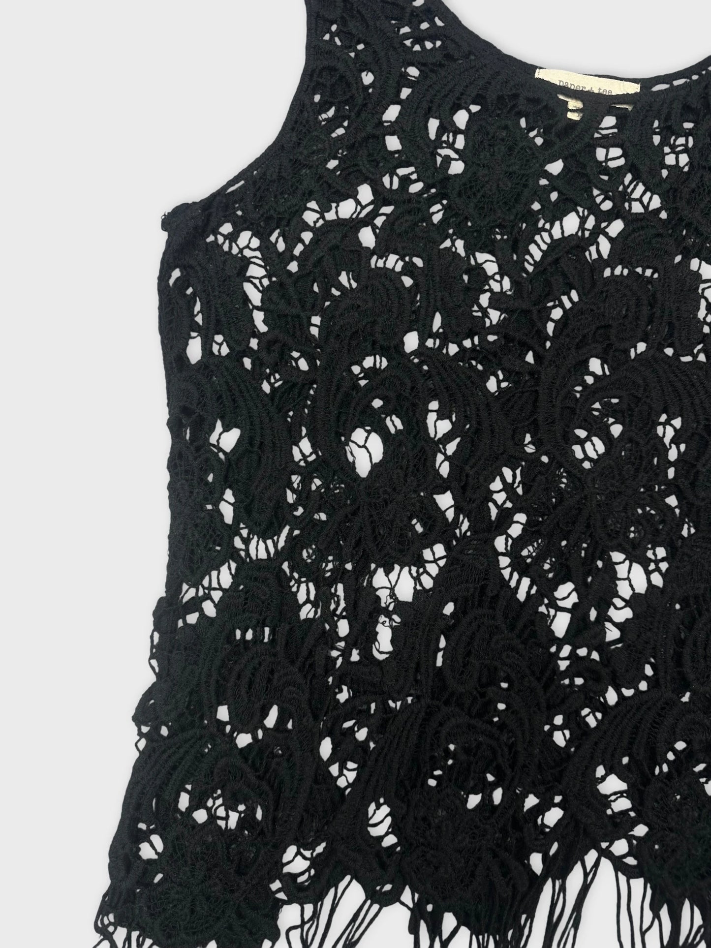 Detail view of a black lace top with intricate pattern and fringed hem.