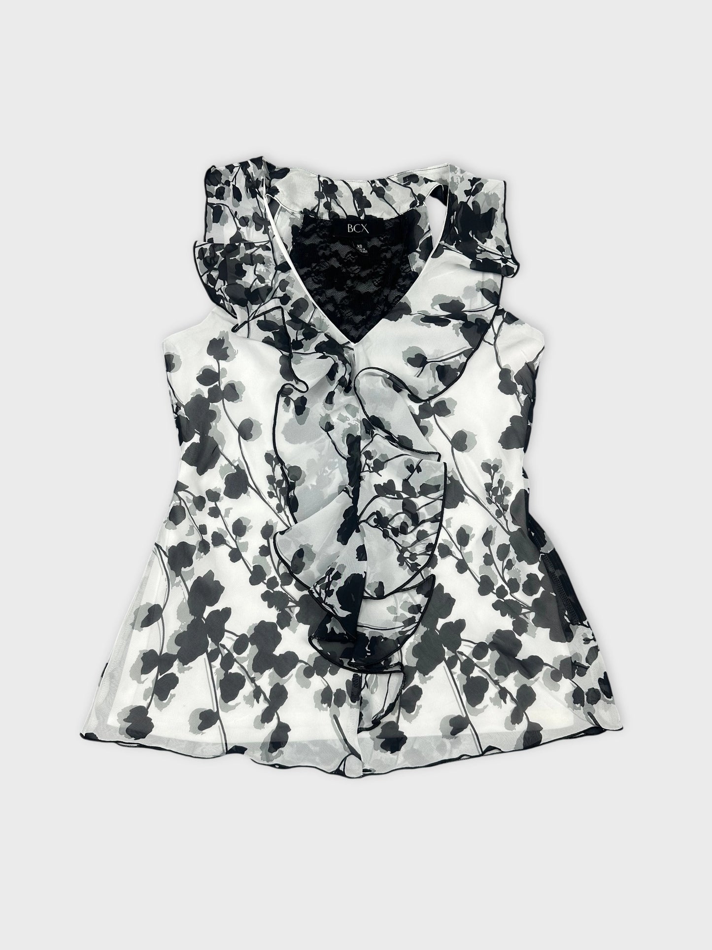 Front view of a sleeveless black and white floral top with ruffled trim.