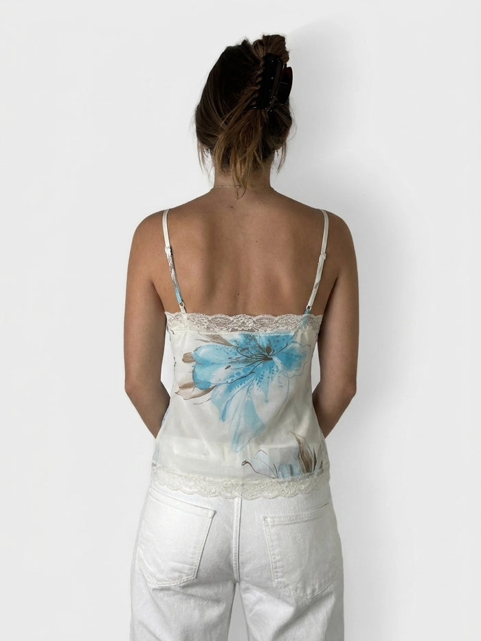 Back view of a light cream upper body top featuring blue floral print and lace trim.