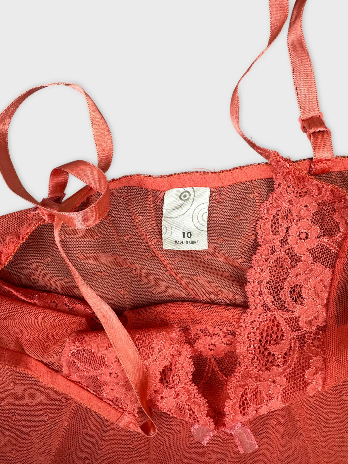 Detail view of a coral sheer lace camisole with ribbon straps.